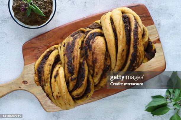 image en gros plan de pain tressé babka salé cuit au four et fait maison aromatisé au pesto sur une planche à pain en bois, bol de tapenade d’olive, fond effet marbre, vue surélevée - tressé photos et images de collection