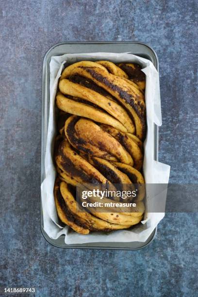 bild einer mit fettdichtem pergamentpapier ausgekleideten antihaft-laibdose mit gebackenem, hausgemachtem, herzhaftem babka-geflochtenem brotlaib, der mit pesto aromatisiert ist, grauer hintergrund gesprenkelt, erhöhte ansicht - hefe stock-fotos und bilder