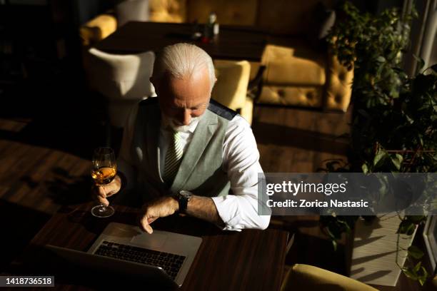 mature businessman drinking wine in a restaurant looking on wristwatch - gentlemens club stock pictures, royalty-free photos & images