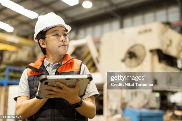 a shop floor control for operations management in the automobile industry. a japanese production manager holds a tablet computer while standing in a factory surrounded by press stamping machinery to monitor production overall processes. - operations manager stock pictures, royalty-free photos & images