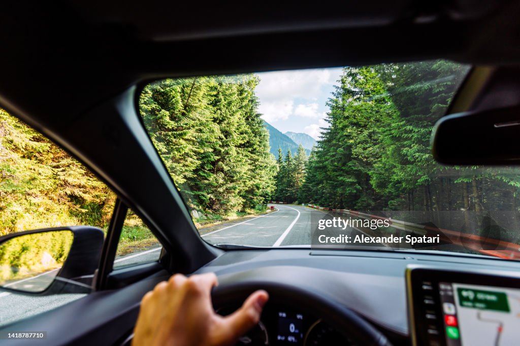 Man driving on the mountain road surrounded by forest, personal perspective view