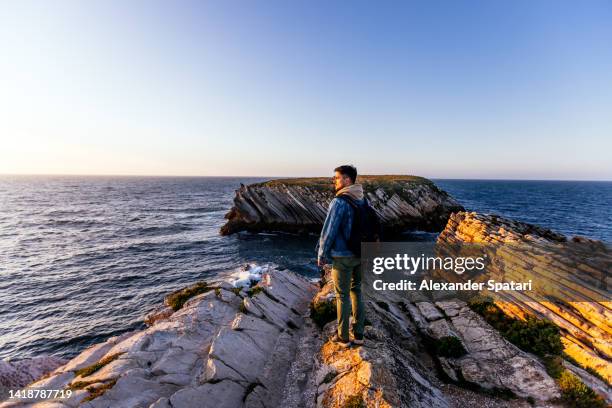 man standing on the edge of the cliff, looking at the sunset by the ocean on baleal, peniche - wonderlust stock pictures, royalty-free photos & images