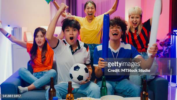 eine gruppe glücklicher asiatischer teenager sitzt auf der couch und schaut sich nachts im fernsehen fußballspiele an. - friends tv show stock-fotos und bilder