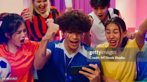 group of happy asia teen sit on couch watch cheer sport online soccer games world cup on cell phone at night. - smartphone euro stockfoto's en -beelden