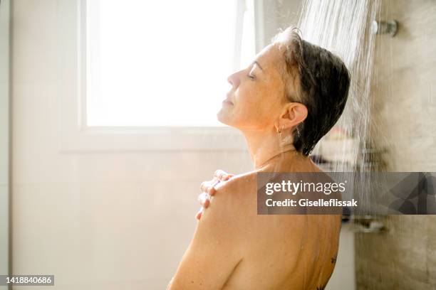 mature woman with a back tattoo taking a relaxing shower at home - woman in shower tattoo stock pictures, royalty-free photos & images