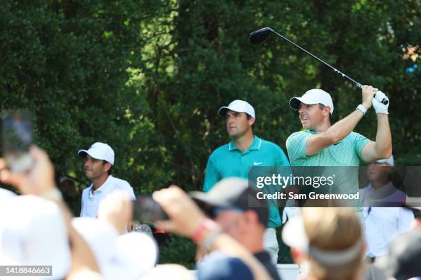 Rory McIlroy of Northern Ireland plays his shot from the 13th tee as Scottie Scheffler of the United States looks on during the final round of the...