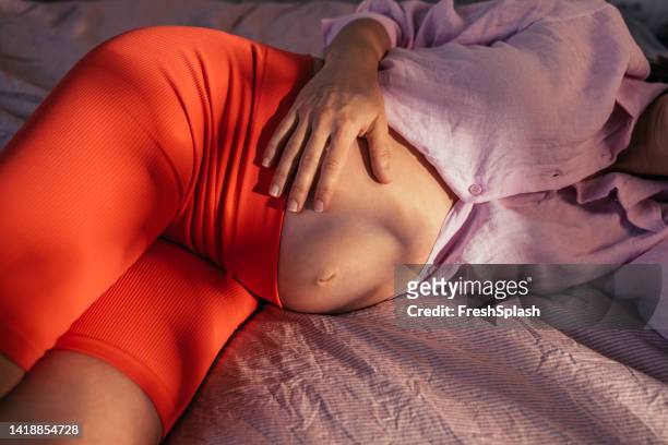 eine nahaufnahme einer unkenntlich schönen schwangeren frau, die sich zu hause entspannt - woman holding tummy stock-fotos und bilder