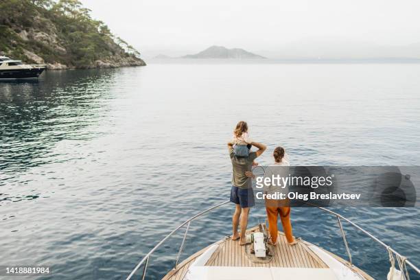view from behind of happy family travelling with baby on board of luxury yacht. unrecognizable people - rijk stockfoto's en -beelden