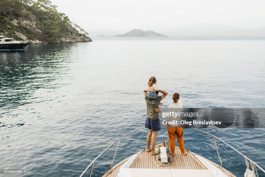 View from behind of happy family travelling with baby on board of luxury yacht. Unrecognizable people