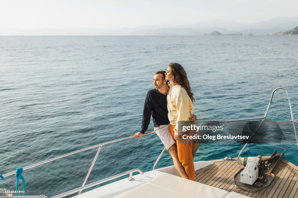 Young couple hugging and enjoying evening on board of luxury yacht. Sailing adventures, travel aboard
