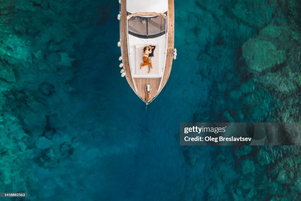 Aerial drone view of couple in love on board of luxury yacht anchored in tropical paradise bay with emerald clear water