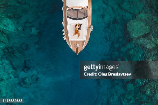 Aerial drone view of couple in love on board of luxury yacht anchored in tropical paradise bay with emerald clear water Aerial drone view of couple in love on board of luxury yacht anchored in tropical paradise bay with emerald clear water