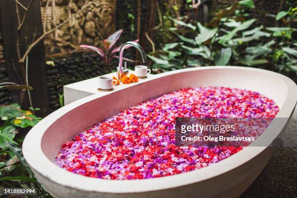 stone bath tub full of flower petals in balinese relaxation spa. wellness and vitality - bali luxury stock pictures, royalty-free photos & images