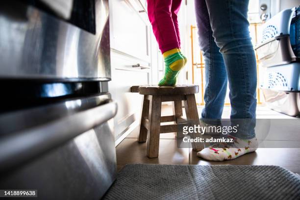little girl standing on tippy toes on a stool to reach the counter - capitalism stock pictures, royalty-free photos & images