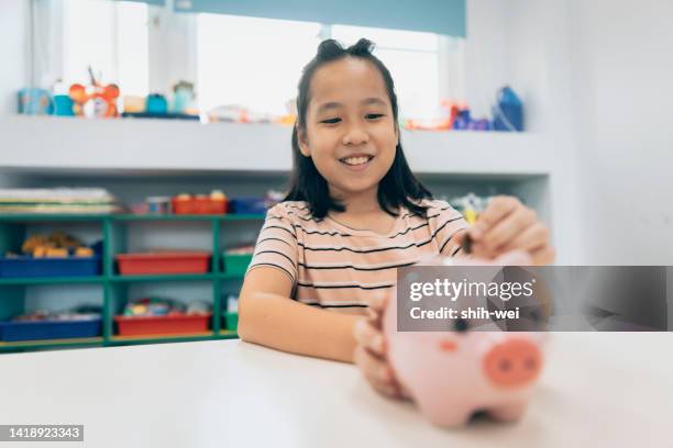 girl putting coin into piggy bank - kids making money stock pictures, royalty-free photos & images