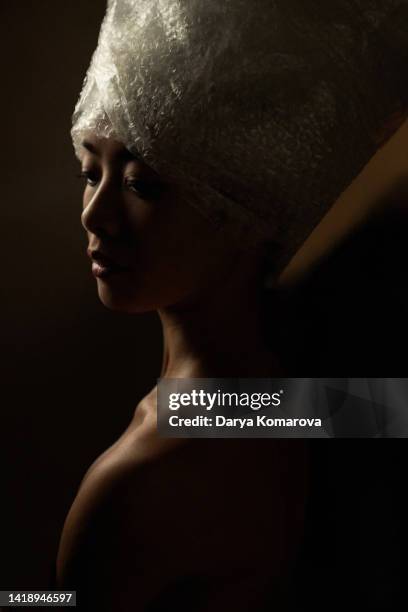 a japanese young woman looks down in the image of nefertiti on a black background. - queens head stock pictures, royalty-free photos & images