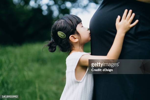 close up of lovely little asian girl embracing and kissing her pregnant mother's belly in the nature. sibling love. welcoming a new family member. expecting a new life with love and care. sharing love concept - little kids belly imagens e fotografias de stock