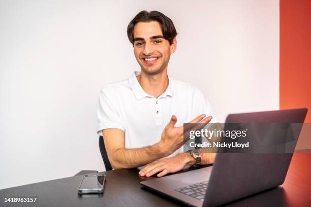 porträt eines lächelnden jungen geschäftsmannes, der mit laptop am tisch sitzt - young man white tshirt stock-fotos und bilder