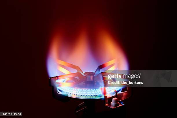 close-up of gas stove burner with burning gas against dark red background - camping stove stockfoto's en -beelden