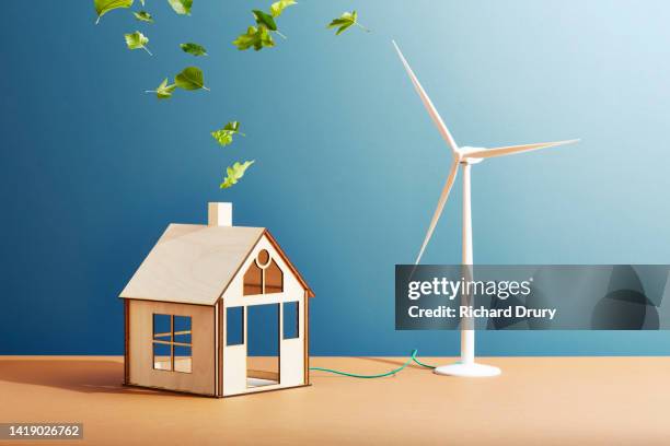 a wooden house with a wind turbine and leaves and flowers coming out of the chimney - huella de carbono fotografías e imágenes de stock