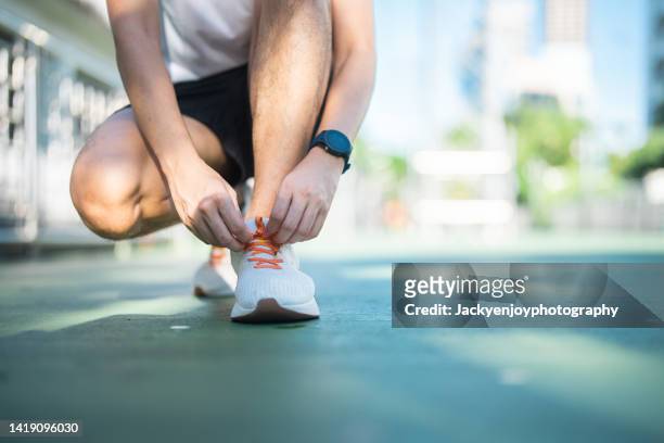close-up man tying running shoes shoelace before jogging in a park - shoelace stock pictures, royalty-free photos & images