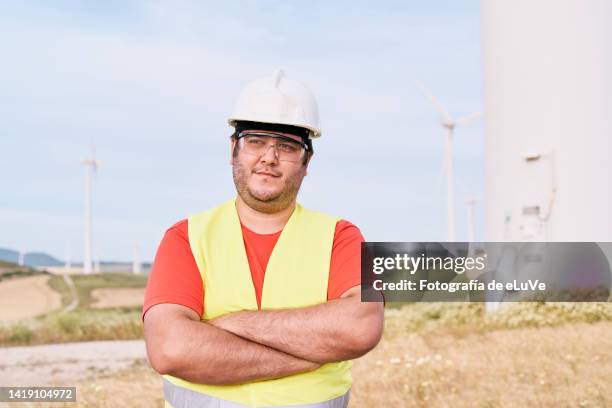 portrait of young male engineer worker standing at solar eolic power station in front of a turbine with crossed arms - südeuropäischer abstammung stock-fotos und bilder