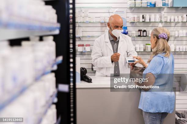 pharmacist with protective mask and senior customer discuss medication - pharmacy mask stock pictures, royalty-free photos & images