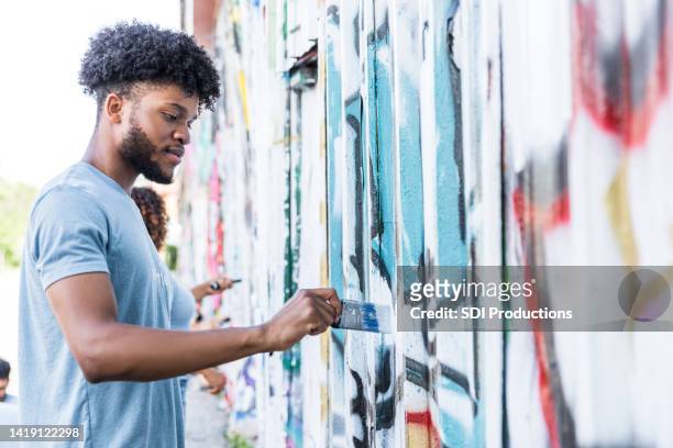 low angle view male student painting over graffiti - altruismo stock pictures, royalty-free photos & images