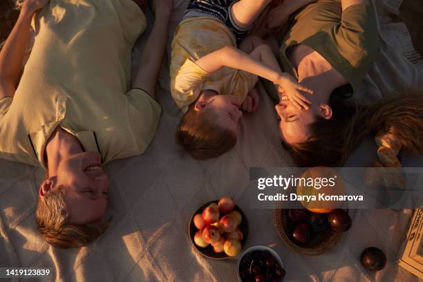 a family of three is having fun on the beach on the picnic blanket. - camel colored stock pictures, royalty-free photos & images