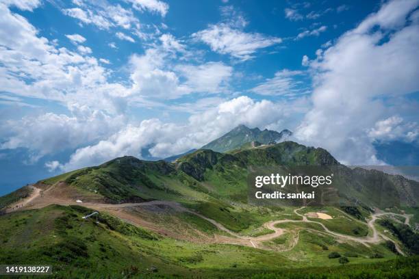 aerial view of winding dirt road in the mountains and mountain ridge at sunny day - russia travel stock pictures, royalty-free photos & images