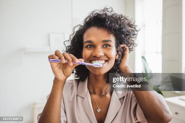 smiling woman brushing healthy teeth in bathroom - teeth cleaning stock pictures, royalty-free photos & images