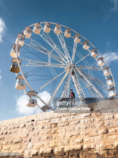 low angle pov of man on top of wall with ferris wheel in the back - ferry wheel stock pictures, royalty-free photos & images