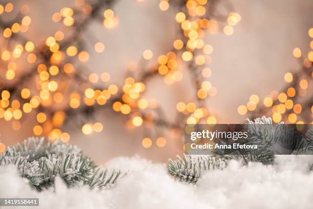 fir tree branches with snow on light background with many yellow and orange illuminating garlands. festive decorations as symbol of coming christmas and new year. bright backdrop for your design - tannenzweig stock-fotos und bilder