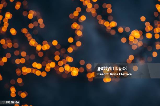 defocused garland with golden lights on blue background. festive lights as symbol of coming christmas and new year. backdrop for your design - christmas dark stock pictures, royalty-free photos & images