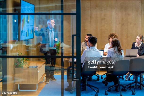 reifer mann, der eine big-data-präsentation auf einem fernseher in einem sitzungssaal hält. - presenting data business stock-fotos und bilder