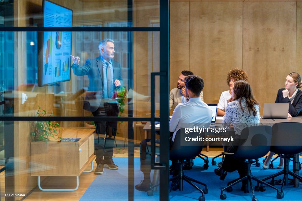 Uomo maturo che fa una presentazione di big data su una tv in una sala riunioni.