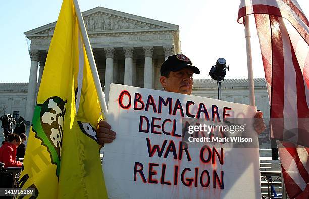 Ron Kirby holds a sign while marching in protest of the Patient Protection and Affordable Care Act in front of the U.S. Supreme Court on March 26,...