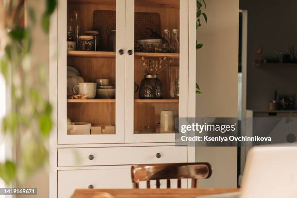 opened white glass cabinet with clean dishes and decor. scandinavian style kitchen interior. organization of storage in kitchen. - cabinet stock pictures, royalty-free photos & images