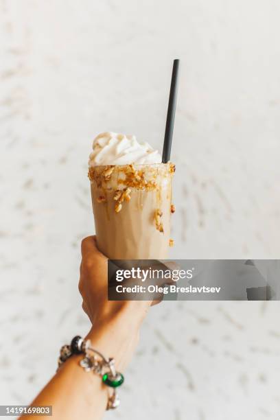 hand holding milkshake cocktail with caramel on side and whipped cream on top. white background - ice coffee drink stock pictures, royalty-free photos & images