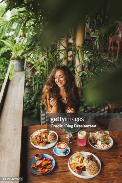 young woman enjoying breakfast in cafe with various delicious  vegetarian food - burger and chips fotografías e imágenes de stock