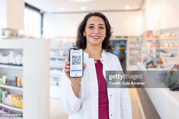 woman pharmacist holding a digital prescription up to the view using her smart phone - doctor using smartphone stock-fotos und bilder