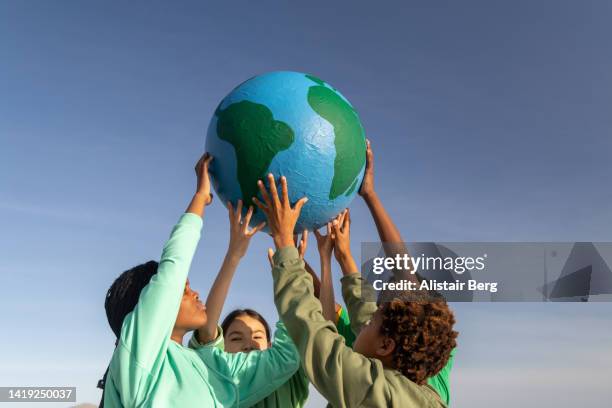 group of children working together to hold up the world - sostenibilidad fotografías e imágenes de stock