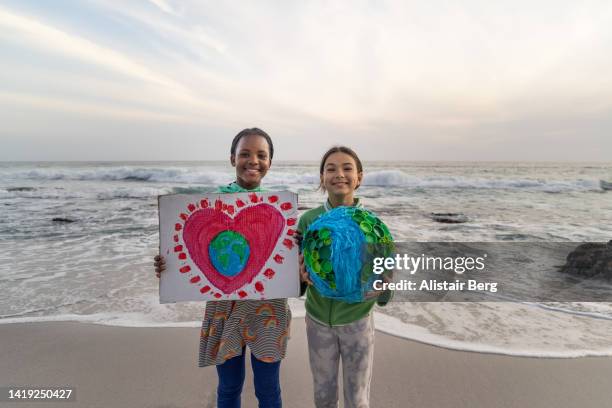 two girls  holding environmental art on a beach at sunset - person holding up sign stock-fotos und bilder