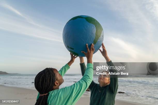 young activists holding globe up on a beach at sunset - world politics stockfoto's en -beelden