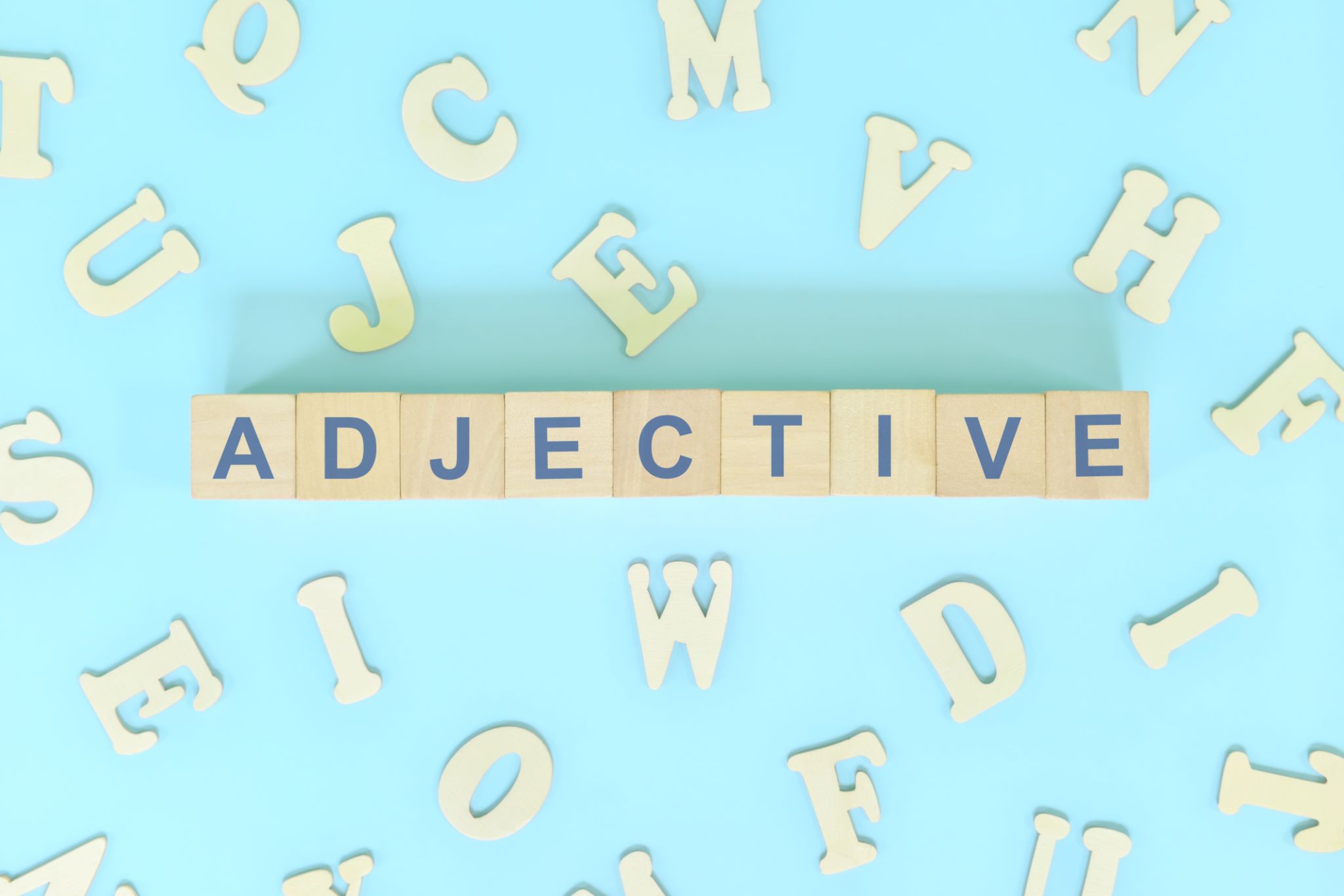 Adjective or adjectives concept in English grammar and learning class lesson. Wooden blocks typography word flat lay in blue background. Adjective or adjectives concept in English grammar and learning class lesson. Wooden blocks typography word flat lay in blue background.