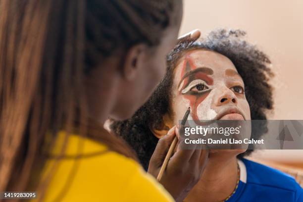 skilled female stage makeup artist using a make up brush and face paint to recreate a scary clown face - scary clown makeup stock-fotos und bilder