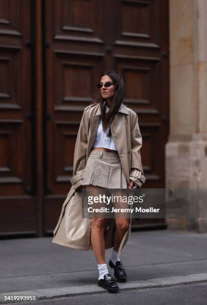 Anna Winter wearing Edited long beige shiny coat, Prada black leather loafer, white socks, Stradivarius beige low waist mini skirt and white cropped...