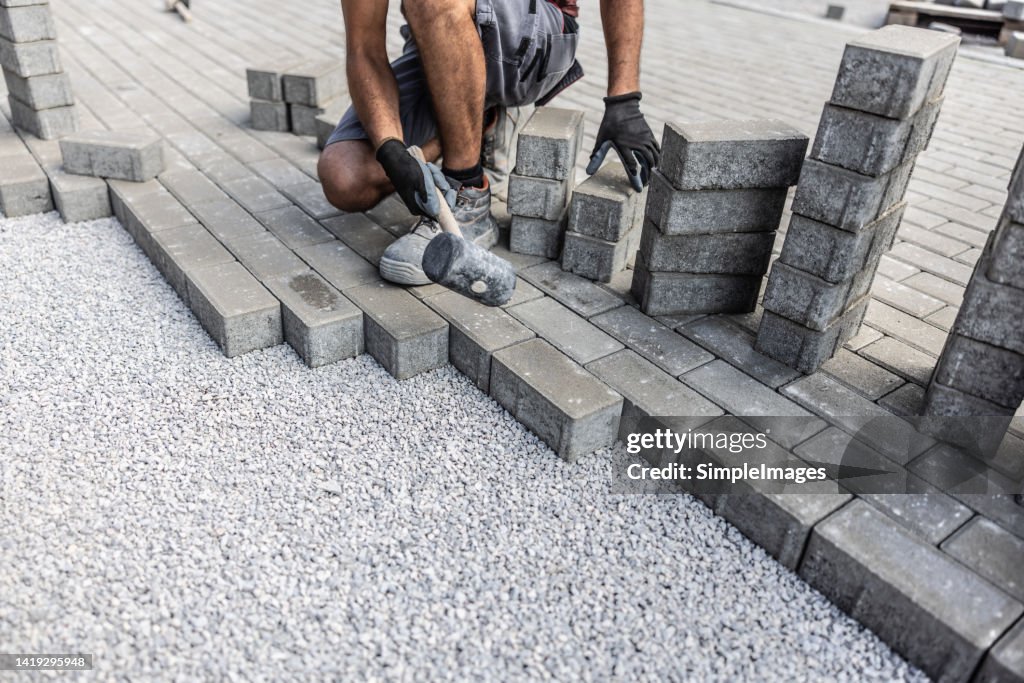 Male construction worker paves the area with concrete grey paving tiles.
