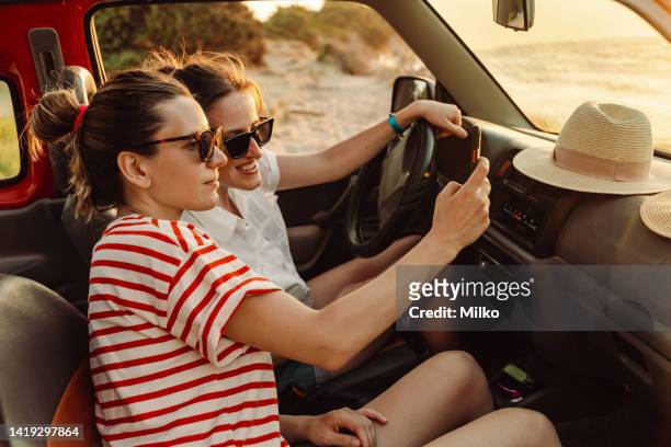 mädchen auf einem sommer-roadtrip und mit dem smartphone - friends inside car stock-fotos und bilder