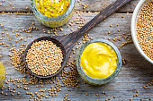 Different types of mustard and mustard seeds on a rustic wooden board